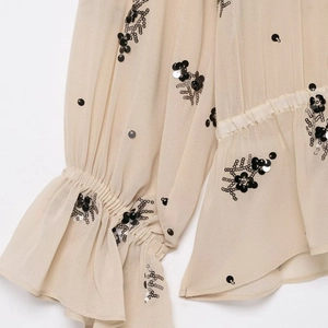 Detail of beige sequin flower embroidery and elastic ruffled cuffs on a sheer shirt