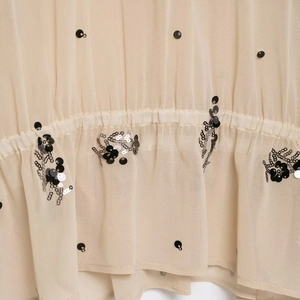 Detailed close-up of beige sheer chiffon fabric with black sequins and silver embroidery