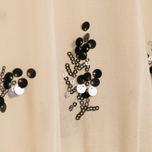 Macro detail of sequin floral embroidery on a translucent champagne chiffon shirt