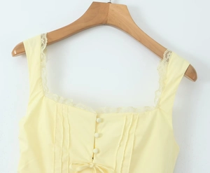Détail du décolleté carré avec dentelle cils et plis boutonnés sur la robe jaune