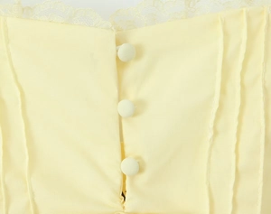 Vue détaillée d'une robe jaune clair avec bordure en dentelle, plis et boutons en tissu