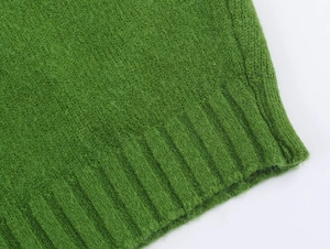 Macro shot of green knitted sweater detailing ribbed hem texture and soft fabric finish
