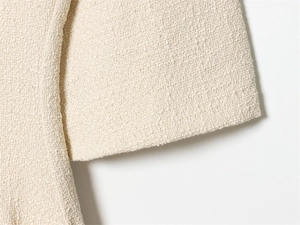 Macro detail of off-white tweed fabric texture and stitching on casual dress sleeve