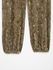 Detail of velvet trousers featuring floral prints and elastic cuffs with metallic sheen