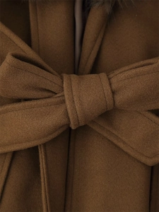 Detail of wool coat featuring a faux fur collar and decorative bow belt in brown