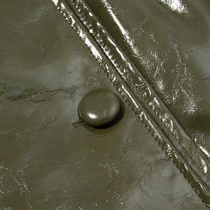 Close-up of olive green glossy leather fabric with matching button and quilted texture