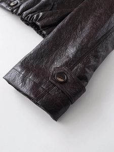 Detail of dark brown PU leather sleeve with button tab and fine textured stitching