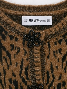 Détail du cardigan léopard avec fleur en perles noires et étiquette de marque tissée