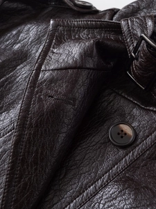 Macro detail of brown PU leather texture, resin button, and collar strap on jacket