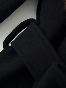 Close-up of belt loop stitching on black wool coat with brown faux fur collar detail