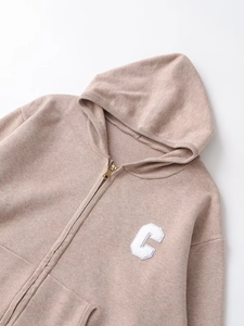 Detail of oatmeal knit hoodie featuring a gold metal zipper and white chenille letter C patch