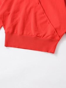 Close-up of red knit sweater featuring ribbed hem and reinforced pocket stitching details