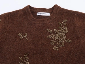 Close-up of floral beadwork and knit texture on a brown crewneck short sleeve sweater