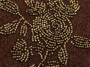 Detailed macro view of bronze floral bead embroidery on brown knit sweater fabric