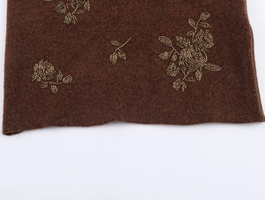 Close-up of brown knit sweater featuring intricate golden bead rose embroidery details