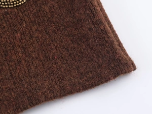 Detail of dark brown knit fabric with decorative gold metal beads along the edge