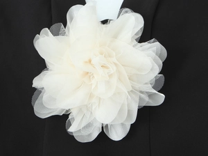 Detail of a beige mesh floral corsage with layered petals on a black fabric background
