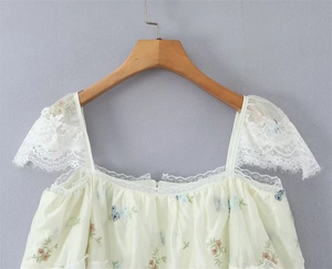 Detail of floral embroidery and delicate white lace trim on a yellow summer top