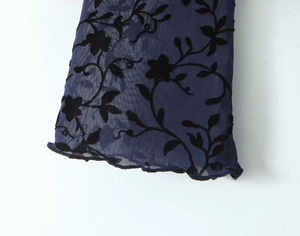 Detail of dark blue mesh dress with black floral flocking and delicate lettuce edges