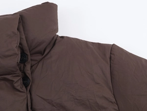 Detailed view of the dark brown stand-up collar and black button on a quilted jacket