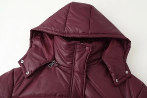 Detail view of burgundy hooded quilted coat showing windproof fabric and metal zipper
