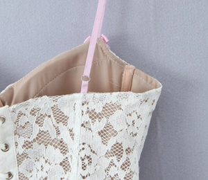 Detail of white floral lace fabric with adjustable pink straps on a slim corset top