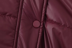 Close-up of deep burgundy quilted jacket featuring a glossy matching snap button detail