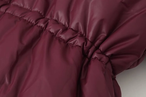 Macro shot of burgundy puffer jacket showing elastic ruched waist and silky fabric texture