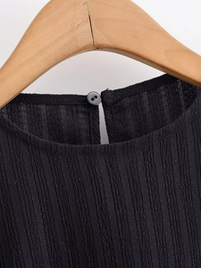 Detail of round neckline with back button closure on a textured black puff blouse