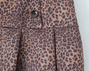 Détail d'une jupe plissée à imprimé léopard avec bouton marron et tissu texturé