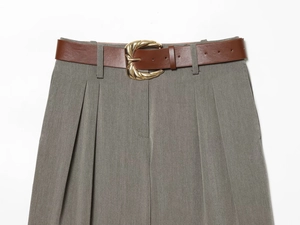 Detail of high-waist grey trousers featuring a brown belt with a gold shell-shaped buckle