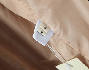 Close-up of beige satin lining with size S and Made in China labels on wool coat