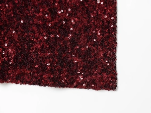 Macro detail of burgundy sequin fabric with reflective metallic texture for evening gown