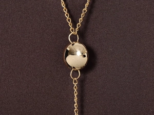Detailed close-up of a polished gold spherical pendant with delicate metal chain link
