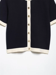 Close-up of navy knit cardigan featuring gold embossed buttons and white contrast trim