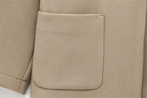 Close-up of camel wool coat showing large patch pocket and textured fabric grain