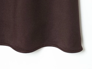Detail of a dark brown dress featuring a scalloped hem with fine stitching craft