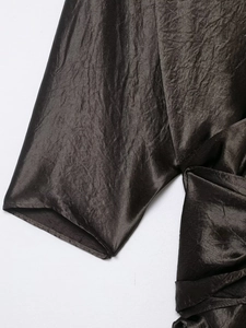 Detail shot of the pleated satin fabric with dark brown sheen on a V-neck dress