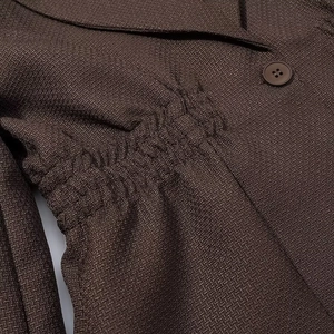 Detail view of dark brown blazer texture with button and elastic waist pleat design