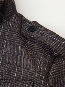 Detail of shoulder epaulette with black button on a brown plaid textured jacket