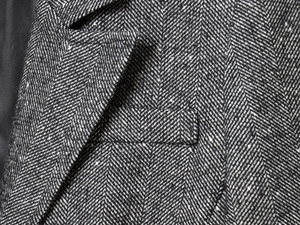 Detail of herringbone wool blazer showing lapel stitching and textured tweed fabric