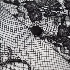 Detail of delicate black floral lace fabric and matching round fabric button on the dress