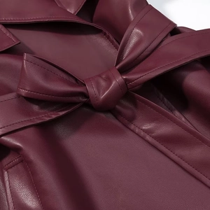 Detail of wine red leather trench coat featuring a tied bow belt and premium grain texture