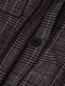 Macro shot of brown plaid fabric detail and a black four-hole button on the winter outfit