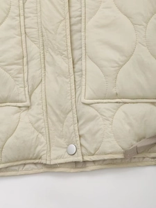 Detail of beige quilted jacket featuring wave stitching and silver snap button