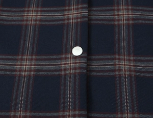 Macro detail of navy plaid fabric with a silver metal snap button and twill texture