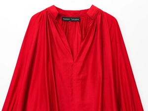 Close-up of a bright red V-neck blouse featuring pleated shoulder details and fabric texture
