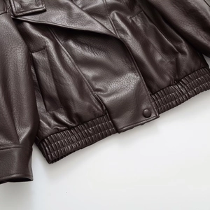 Detail of dark brown faux leather jacket featuring elastic hem and lapel collar texture