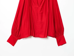 Detail view of red V-neck blouse with puffy lantern sleeves and elegant long pleated cuffs