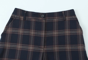 Detail of plaid trousers waist featuring navy check pattern and button closure